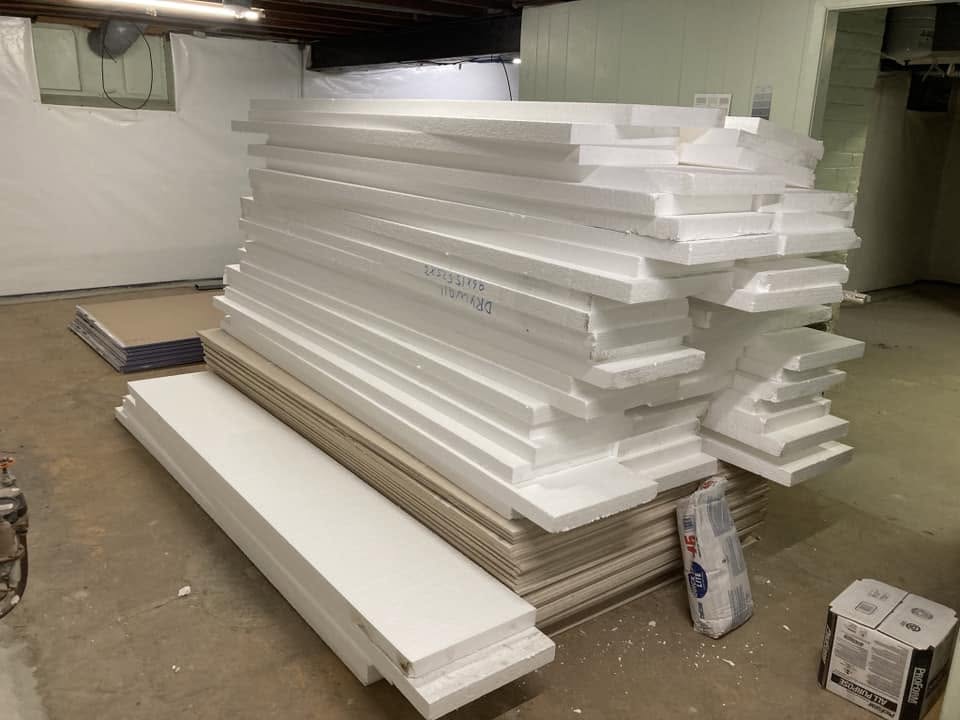 Stacked rigid foam insulation and drywall staged for basement rebuild